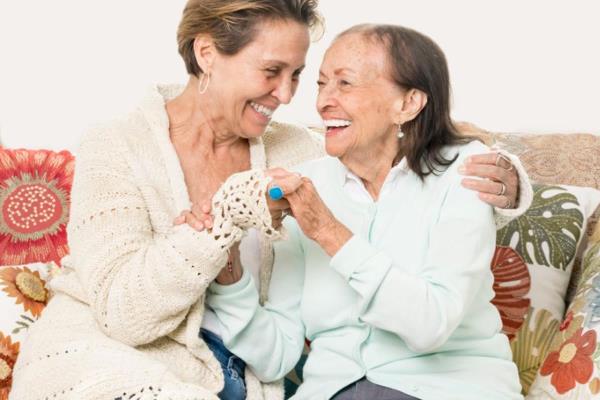 Aging and younger woman laugh and embrace in hug on sofa