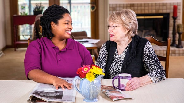Aging woman and care professional enjoy a cup of coffee together at home