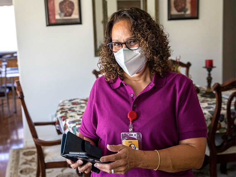 Care professional in home wearing mask and holding mobile phone